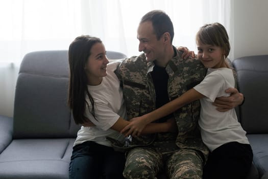 happy positive smiling soldier man in camouflage sitting with his daughter on sofa, looking how his kid grown when he was in army, returning home from war. High quality photo