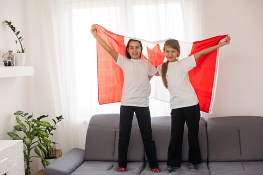 Happy Canada Day Celebration. Two girls with braided hair are at nature background with big Canada flag in their hands. Young Canadian caucasian kids 1st of July. High quality photo
