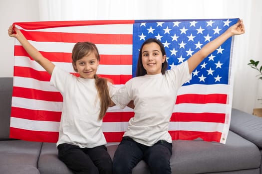 Brunette and blonde teenage girlfriends in white t-shirts holding american flag, energetic teenage friends spending time, friendship. High quality photo