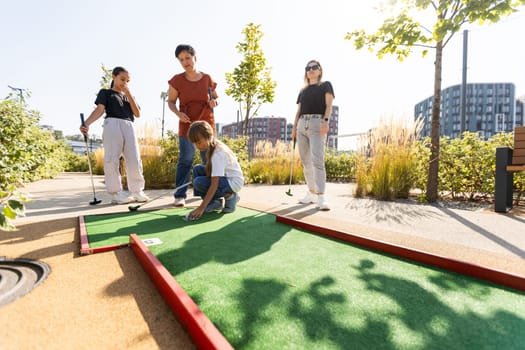 Group of smiling friends enjoying together playing mini golf in the city. High quality photo