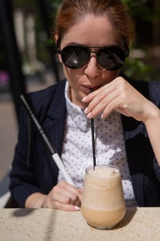 Blind woman in business suit drinking ice coffee in outdoor cafe