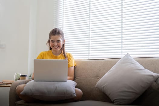 Young woman sitting on the couch and working on project, watching movie on laptop rest and happy chatting with friend in social network at home.