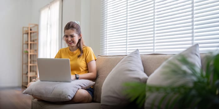 Young woman sitting on the couch and working on project, watching movie on laptop rest and happy chatting with friend in social network at home.