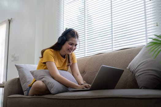 Happy woman wearing headphones watching and listening video on laptop and listening music sitting on a couch at home.