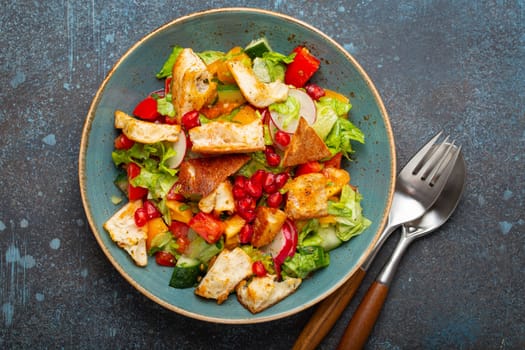 Traditional Levant dish Fattoush salad, Arab cuisine, made with pita bread croutons, vegetables and herbs. Healthy Middle Eastern vegetarian salad on plate, rustic dark blue background top view.