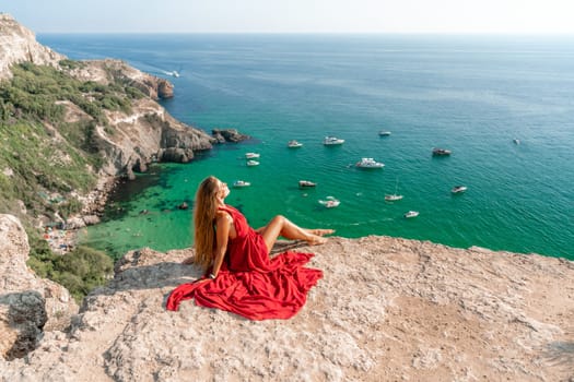 Woman sea red dress yachts. A beautiful woman in a red dress poses on a cliff overlooking the sea on a sunny day. Boats and yachts dot the background