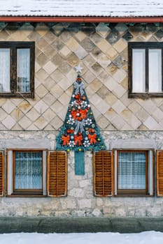 Felt Christmas tree with red bows and garlands hangs on the facade of the house. High quality photo