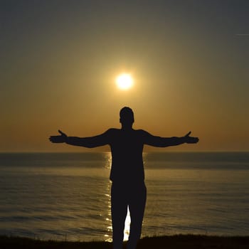 Silhouette of man enjoying freedom with open hands on sea