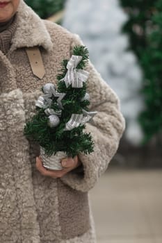 A woman in a fur coat holds a small artificial Christmas tree in her hands