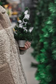 A woman in a fur coat with a small artificial Christmas tree in her hands in a store
