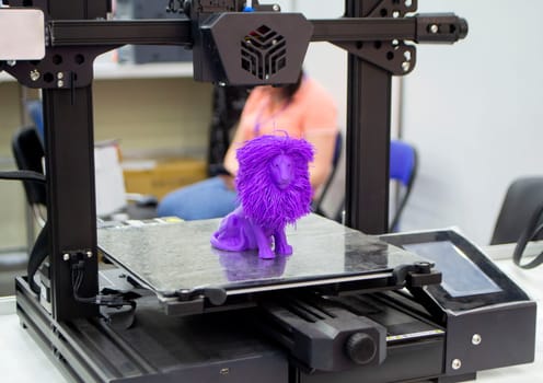 Model of toy lion printed on 3D printer from melted plastic purple color on desktop of 3D printer. Concept 3D printer, 3D printing, modeling prototyping three dimensional object. Innovative production