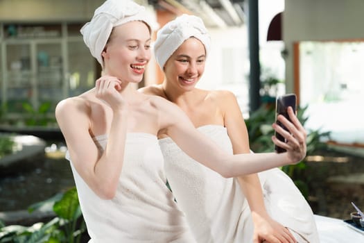 Couple of young beautiful women with beautiful skin in white towel taking a photo together at outdoor surrounded by peaceful natural environment. Beauty and healthy spa concept. Tranquility.