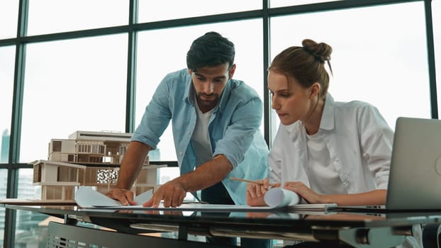 Smart architect engineer inspect house model while colleague using laptop analysis data. Professional designer team working together to design house model construction at modern office. Tracery