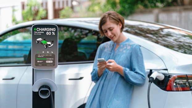 Electric vehicle recharging battery from home EV charging station using alternative energy with net zero emission on blurred background of young girl charging her car before vacation travel. Perpetual