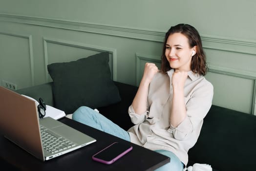 Winning and celebrating. Smiling woman gesturing in a successful video chat on her laptop. Happy woman in glasses is beaming as she communicates on her laptop, signalling victory and success