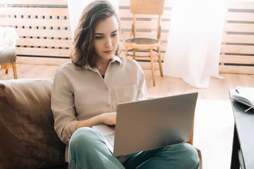 Productive Home Workspace. Woman Typing on Laptop in Living Room. Home Office Vibes: Serious Woman Typing on Laptop in Living Room