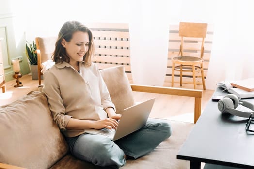 Vivacious Woman in the Living Room. Typing on Laptop with Energy A vivacious woman is typing on a laptop, sitting on the sofa in the living room. Sofa Workstation. Energetic Woman Typing on Her Laptop