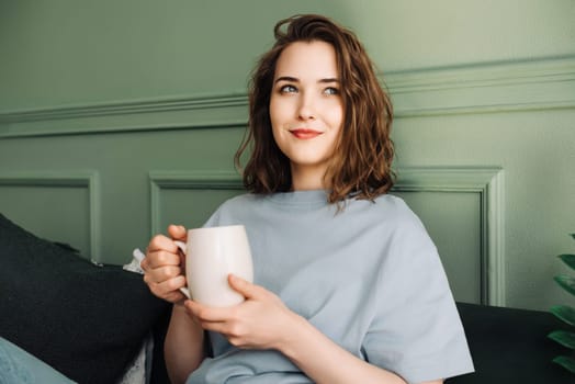 A thoughtful smiling middle-aged woman, enjoying a break and a cup of tea, looks at the vacant space. Pensive Break. Smiling Middle-aged Woman Enjoys Tea, Gazing at Empty Space.