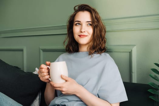 Cosy Tea Time - Close-up of a woman enjoying tea on a sofa in a living room. Relaxed domestic scene, relaxing in an interior setting. Female hands holding a cup of tea or coffee