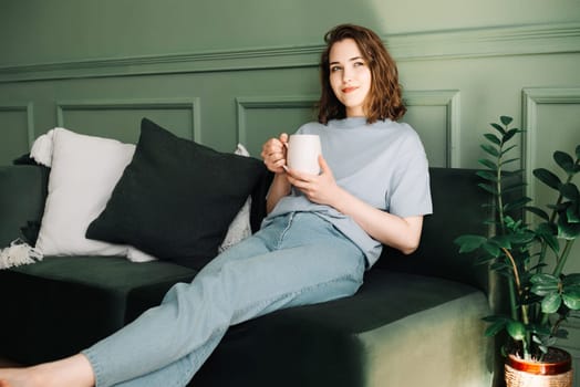 Relaxed Young Woman Reflecting with Tea/Coffee in Home Setting. Serene Mood and Introspection in Cozy Indoor Ambiance. Confident Solitude and Peaceful Demeanor in Tranquil Surroundings