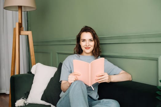 Happy young woman reading a book sitting comfortably on the couch enjoying a relaxing evening. Relaxed young woman enjoying a relaxing evening reading sitting on the couch. Rest and relaxation.