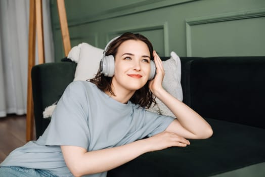 Chill Time. Cheerful Woman Listening to Music on Sofa with Wireless Headphones. Leisure Moments. Content Woman on Couch Listening to Music via Wireless Headphones.