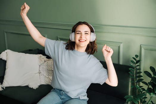 Joyful millennial young woman wearing wireless headphones listening to music, dancing, and enjoying her free time. Carefree Melodies. Joyful Young Woman Dancing to Music.