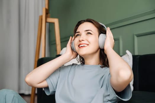 The face of a happy young middle-aged woman wearing wireless headphones, listening to music, enjoying her free time. Musical Delight. Content Middle-Aged Woman Embraces Wireless Tunes.