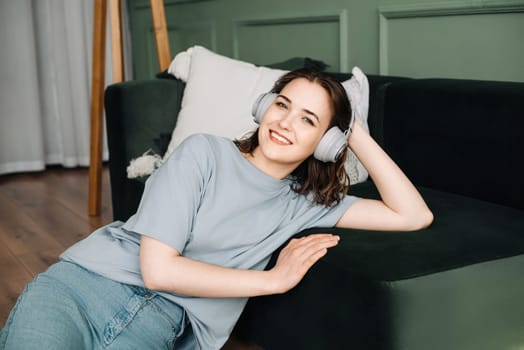 Happy young woman with wireless headphones listening to music on the sofa, enjoying the weekend. Weekend Bliss. Young Woman Delighted in Music with Wireless Headphones.