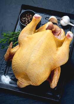 Raw chicken with spices on a stone board on a black background.