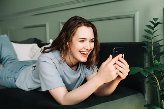 Digital Interaction. Cheerful Woman Socializes, Typing on Smartphone. Relaxed Social Media Time. Happy Woman Engaged on Smartphone, Lying Comfortably.