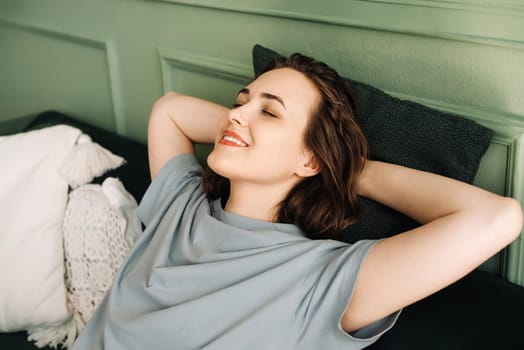 A smiling young woman with her eyes closed is lying on a couch, enjoying some rest and sleep. Serenity Unveiled. Relaxed Young Woman Rests Peacefully on Sofa. Blissful Slumber.