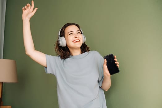 Happy young woman wearing wireless headphones listening to music, enjoying free time, dancing, having fun. Melodic Happiness. Young Woman Grooving to Music in Wireless Headphones.