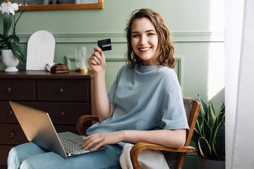 Young Lady Excitedly Using Credit Card for Online Purchase. E-commerce Enthusiasm. Smiling Woman Shows Credit Card with Laptop. Digital Shopping Excitement.