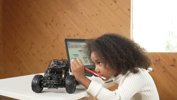 African girl pointing at car model structure while work on laptop. Student inspect at STEM education class. Panorama shot of Clever child using laptop to write programing engineer code. Erudition.