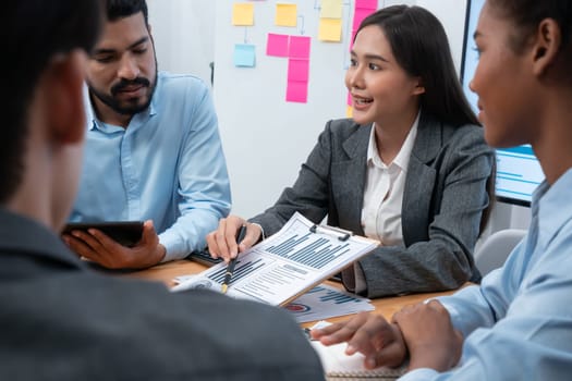 Multiracial analyst team use BI dashboard data to analyze financial report on meeting table. Group of diverse business people utilize data analysis by FIntech for business marketing decision. Concord