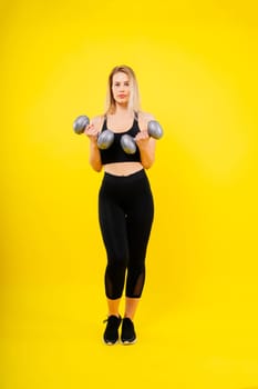 Athletic woman in a sportswear raises dumbbells leads healthy lifestyle has happy expression