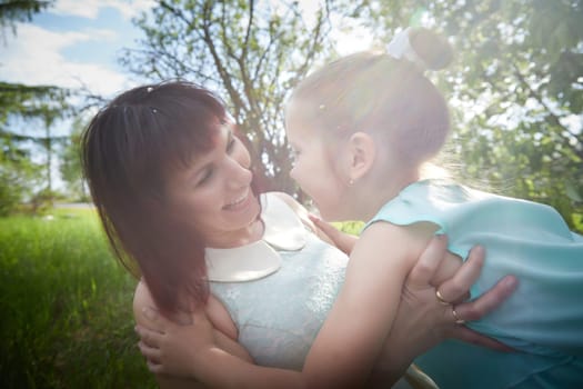 Happy mother and daughter enjoying rest, playing and fun on nature on a green lawn and with blooming apple tree in the background. Woman and girl resting outdoors in summer and spring day