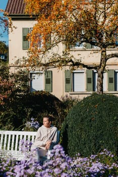 a girl sits on a bench in the park and enjoys the sun. Portrait young adult attractive woman enjoy sitting on bench and relaxing calm carefree rest in city park against green grass and trees on sunny day. Single female person relaxing chilling outdoors