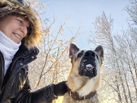 Adult girl with shepherd dog taking selfies in winter forest. Middle aged woman and big shepherd dog on nature in cold day. Friendship, love, communication, fun, hugs