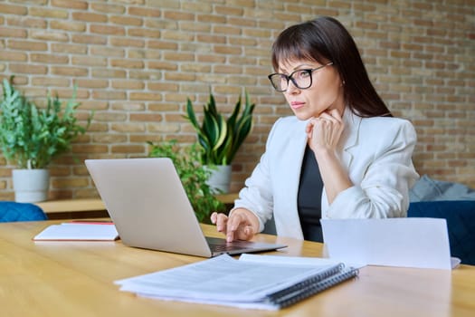 Mature business woman working in office, typing on laptop computer. Business, work, job, management, finance, law, logistics, sales, services concept