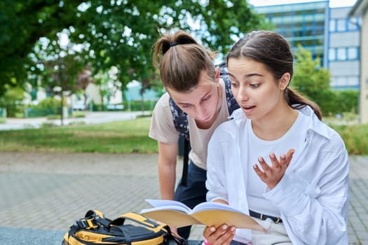 Two high school students guy and girl outdoor, school building background. Education, friendship, youth, adolescence concept