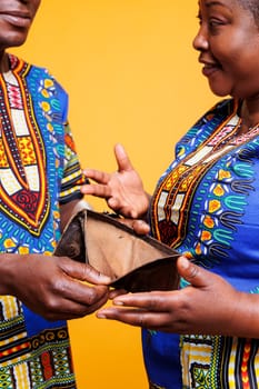 Broke couple discussing bankruptcy and holding purse with no money cash in hands. Smiling black wife showing empty wallet and explaining financial problem to husband closeup