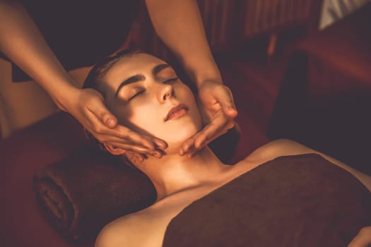Caucasian woman enjoying relaxing anti-stress head massage and pampering facial beauty skin recreation leisure in warm candle lighting ambient salon spa in luxury resort or hotel. Quiescent