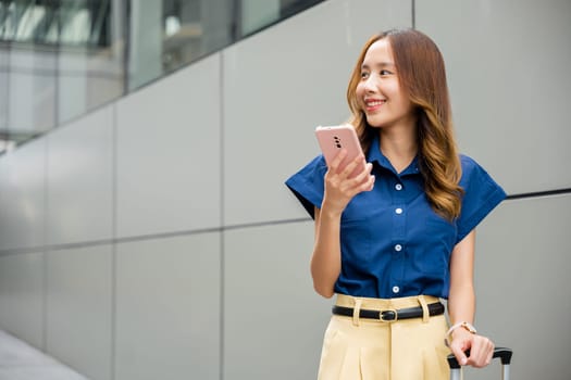 Young female traveler holding mobile phone and using app to track flight status at the airport. Asian travel woman using smartphone app at airport is the focus.