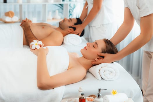 Caucasian couple enjoying relaxing anti-stress head massage and pampering facial beauty skin recreation leisure in dayspa modern light ambient at luxury resort or hotel spa salon. Quiescent
