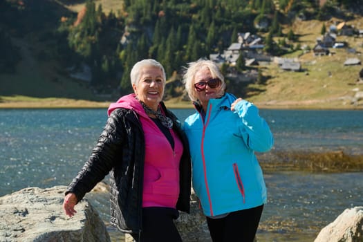 Senior women hikers standing on mountain enjoying a trekking day - Smiling climbing tourists enjoying holidays and healthy lifestyle - Freedom, success sport concept.