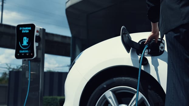 Businesswoman recharge her electric car from charging station at city center or public parking car. Eco friendly rechargeable car using alternative clean energy. Peruse