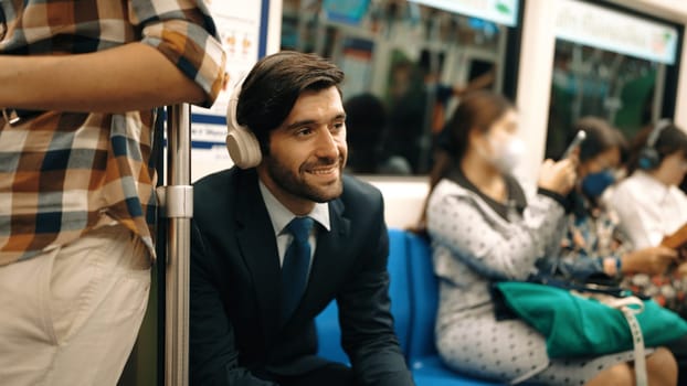 Smiling handsome male investor listening relaxing music while sitting on train. Professional business man enjoy listening music while using public transport to workplace. Blurred background. Exultant.