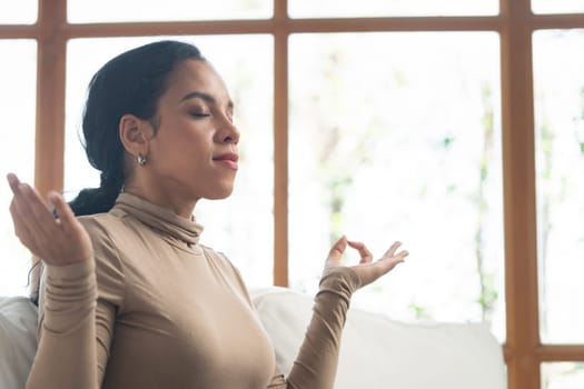 Young African American woman practice crucial mindful meditation at home living room for improving mental health strength and peaceful beautiful living